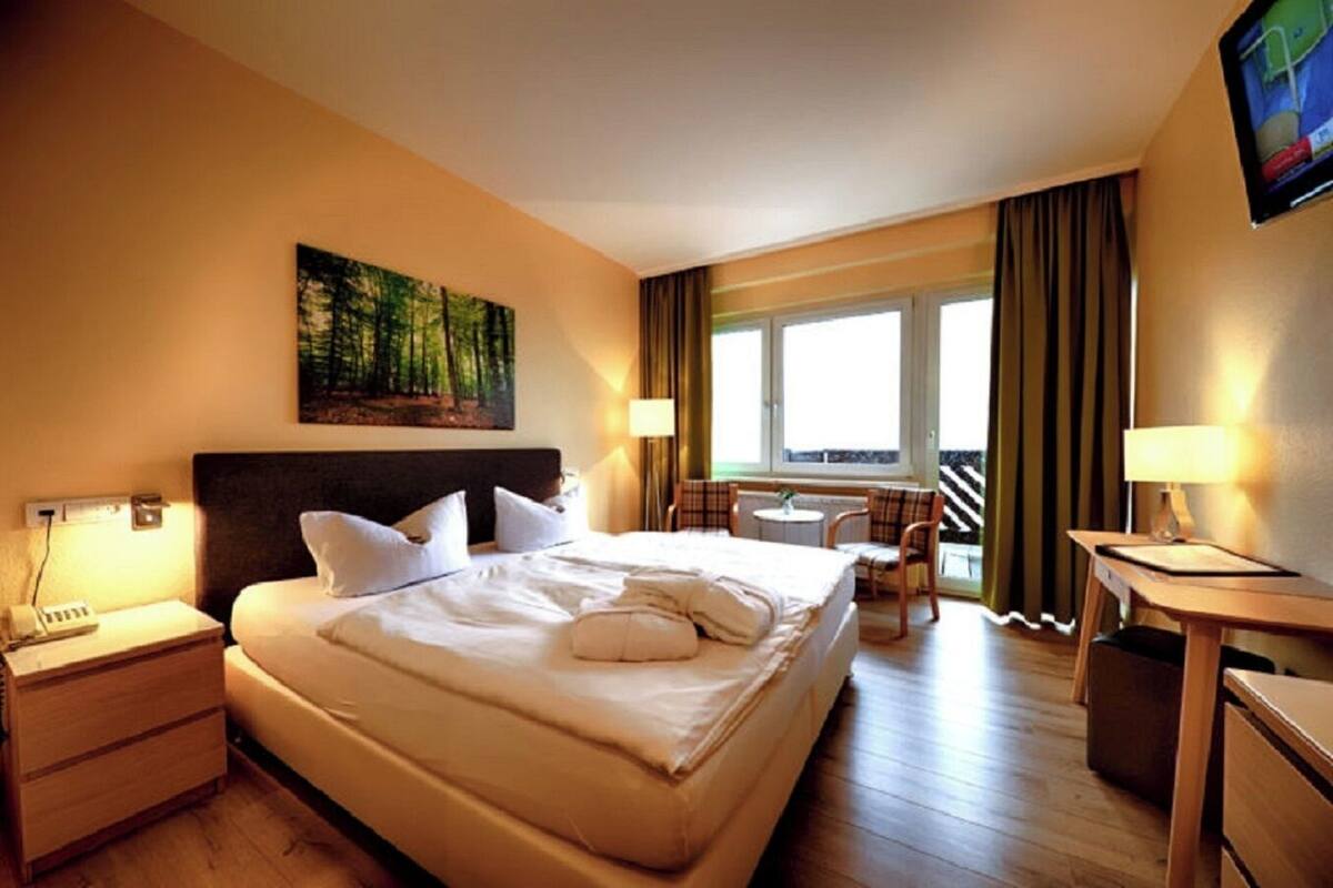 Une chambre d’hôtel avec un grand lit, un bureau, une chaise et une fenêtre avec des rideaux.