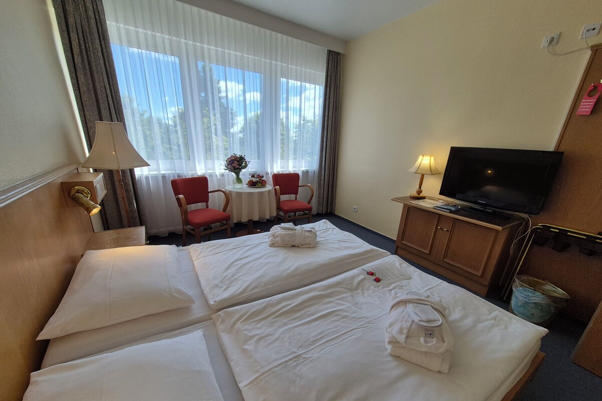 Une chambre d’hôtel avec deux lits, une télévision, un bureau avec une lampe et une fenêtre avec des rideaux.