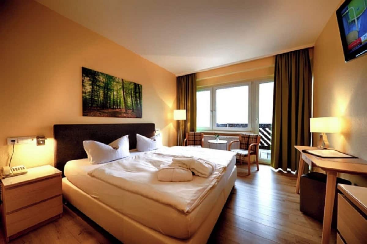 Une chambre d’hôtel avec un grand lit, un bureau, une chaise, une fenêtre avec des rideaux et un tableau au mur.