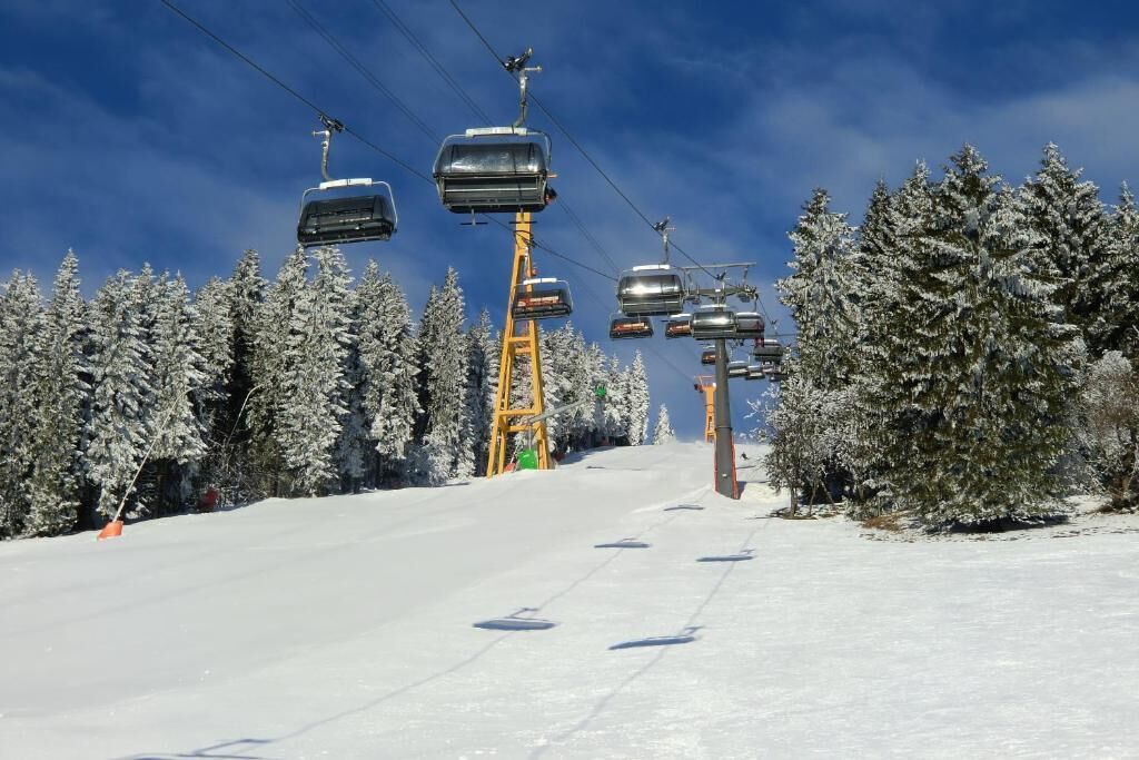A ski lift with chairs moving along a snowy slope, surrounded by snow-covered trees.