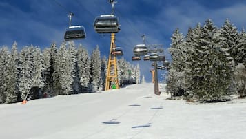 A ski lift with chairs moving along a snowy slope, surrounded by snow-covered trees.