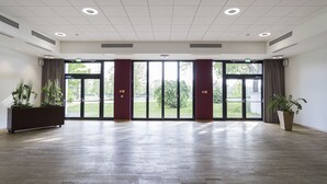 A spacious room with a wooden floor, large windows, and a potted plant. - Hotel am See (Grevesmuehlen)