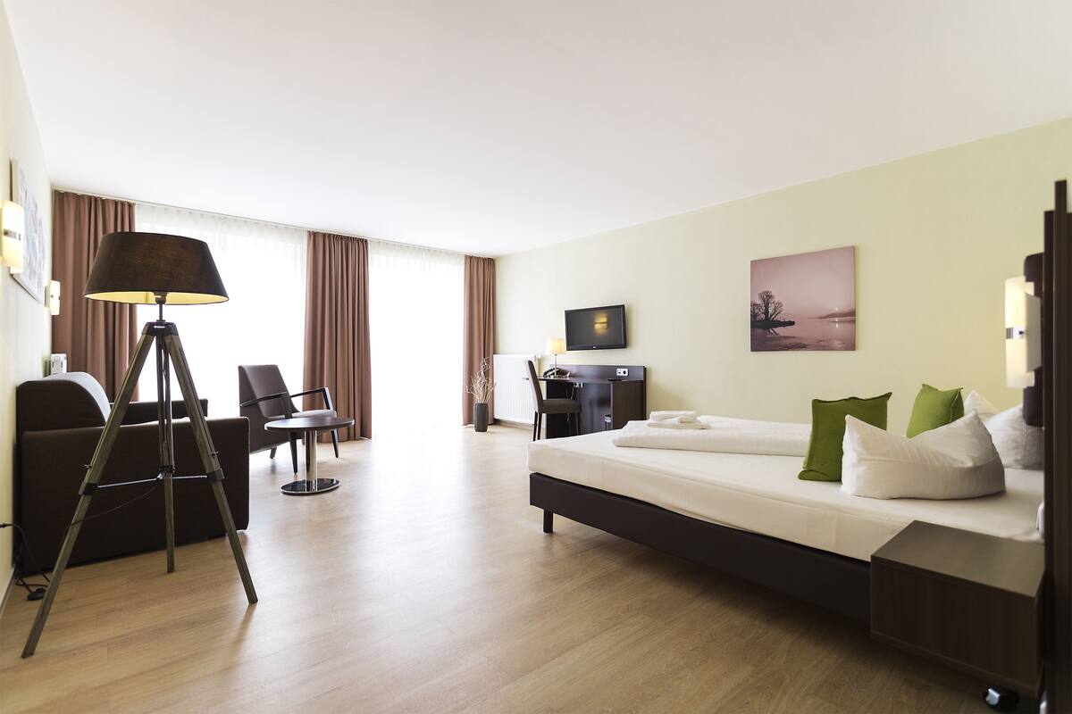A hotel room with a bed, a desk, a chair, and a lamp.