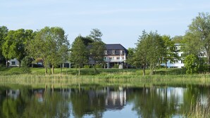 A house with a large front yard and a pond in front. - Hotel am See (Grevesmuehlen)