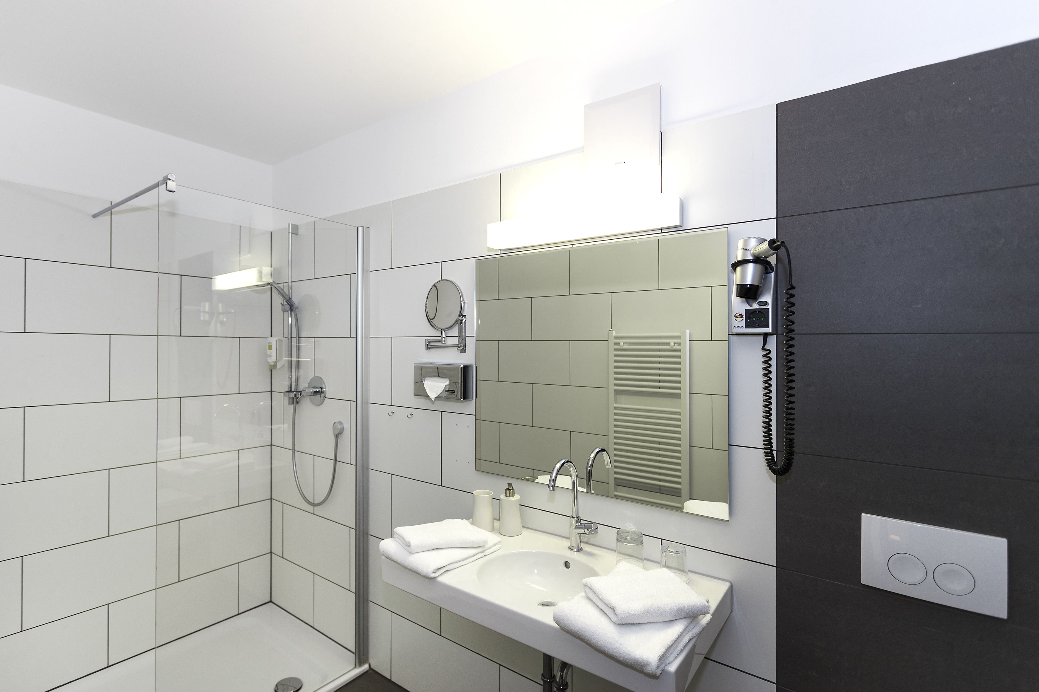 Ein modernes Badezimmer mit einer Duschkabine aus Glas, einem Waschbecken inklusive Spiegel und einem an der Wand befestigten Föhn.