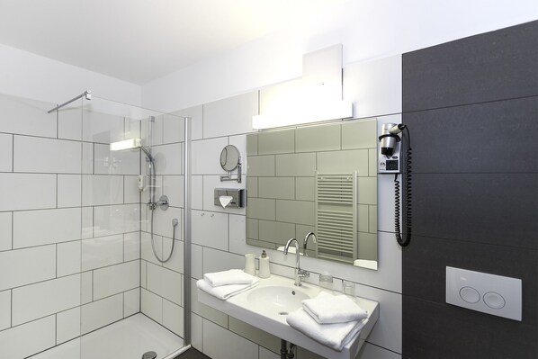 Un baño moderno con ducha de vidrio, un lavabo con espejo y un secador de pelo montado en la pared.