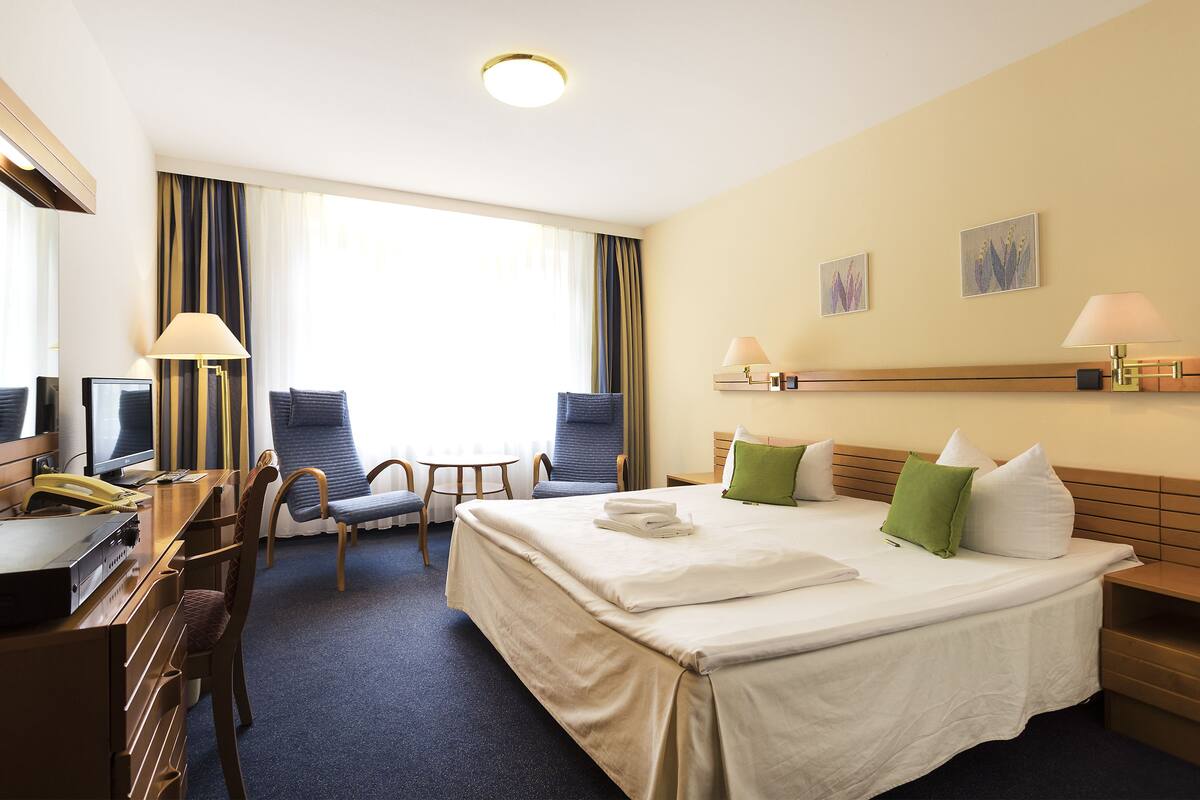 A hotel room with a large bed, two chairs, a desk with a telephone, and a small table.
