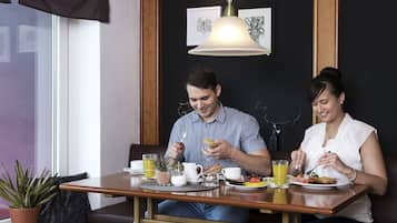 Uma área de jantar com uma mesa posta para dois, com uma xícara de café, um copo de suco de laranja e pratos com comida.