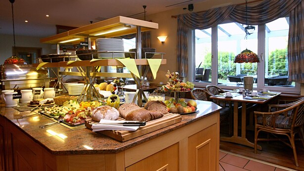 A breakfast buffet with various food items and a seating area with a view of the outdoors. - Hotel am See (Grevesmuehlen)