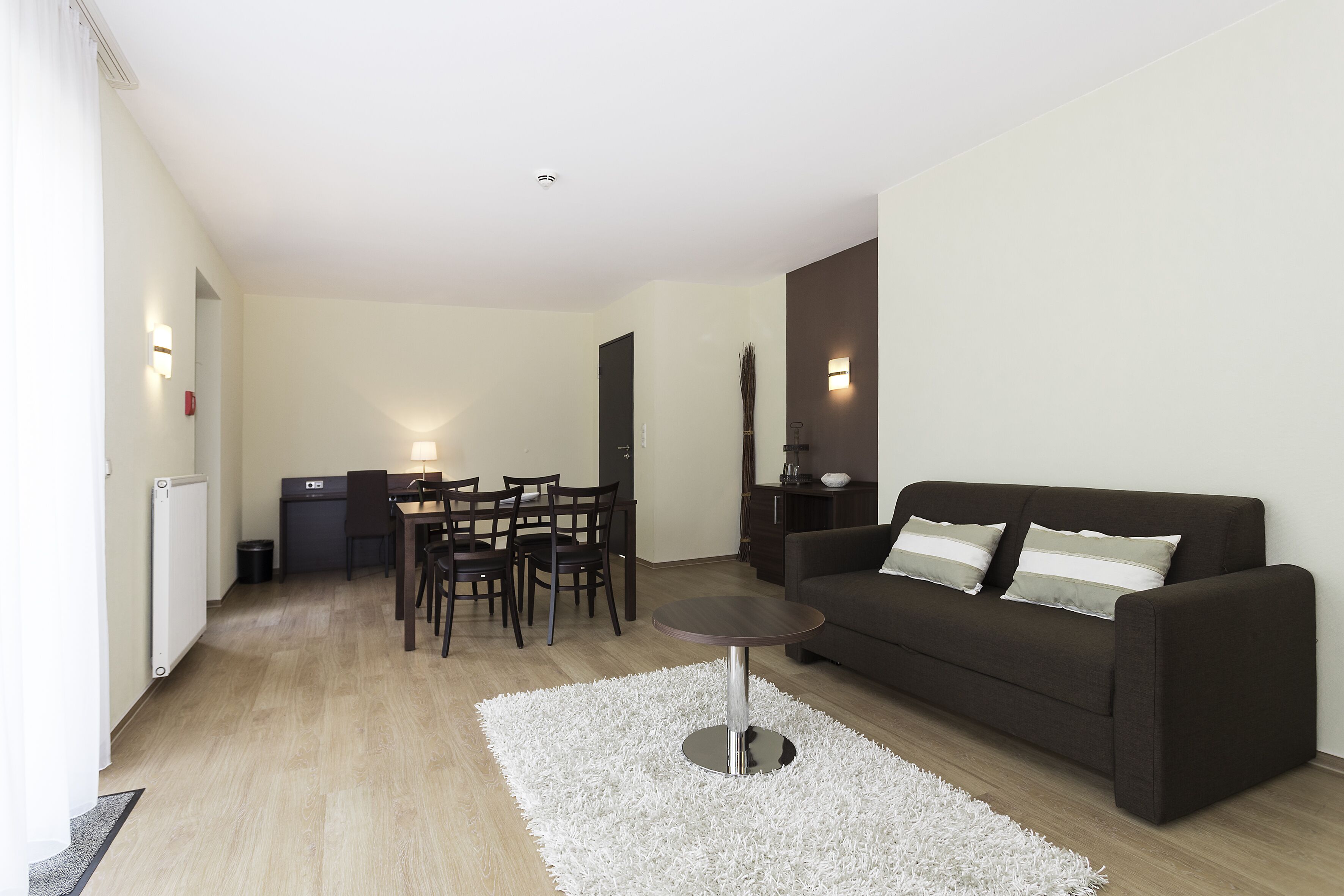 En moderne stue med en mørkebrun sofa, et rundt sofabord og et spiseområde med bord og stole.
