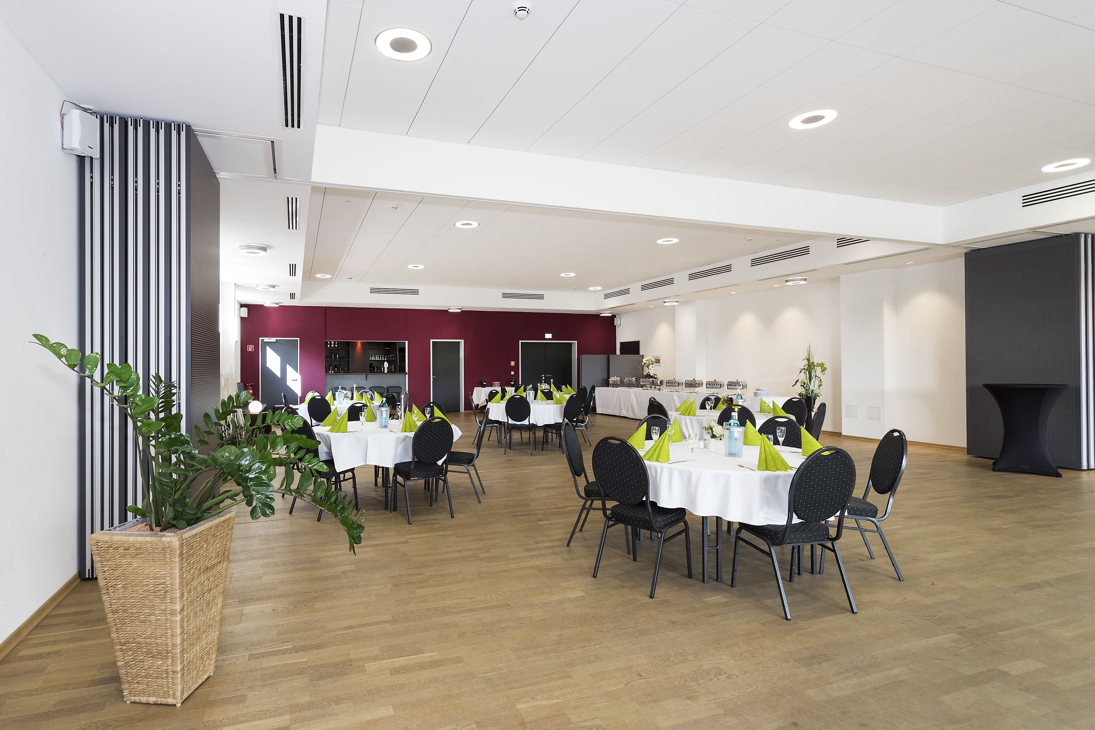 Un vaste espace dédié à la salle à manger, avec plusieurs tables et chaises, une grande plante en pot et un design moderne au niveau du plafond.