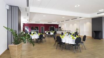 Un vaste espace dédié à la salle à manger, avec plusieurs tables et chaises, une grande plante en pot et un design moderne au niveau du plafond.
