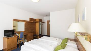 Ein Hotelzimmer mit Bett, Schreibtisch, Computer, Stuhl, Kleiderschrank und Lampe.
