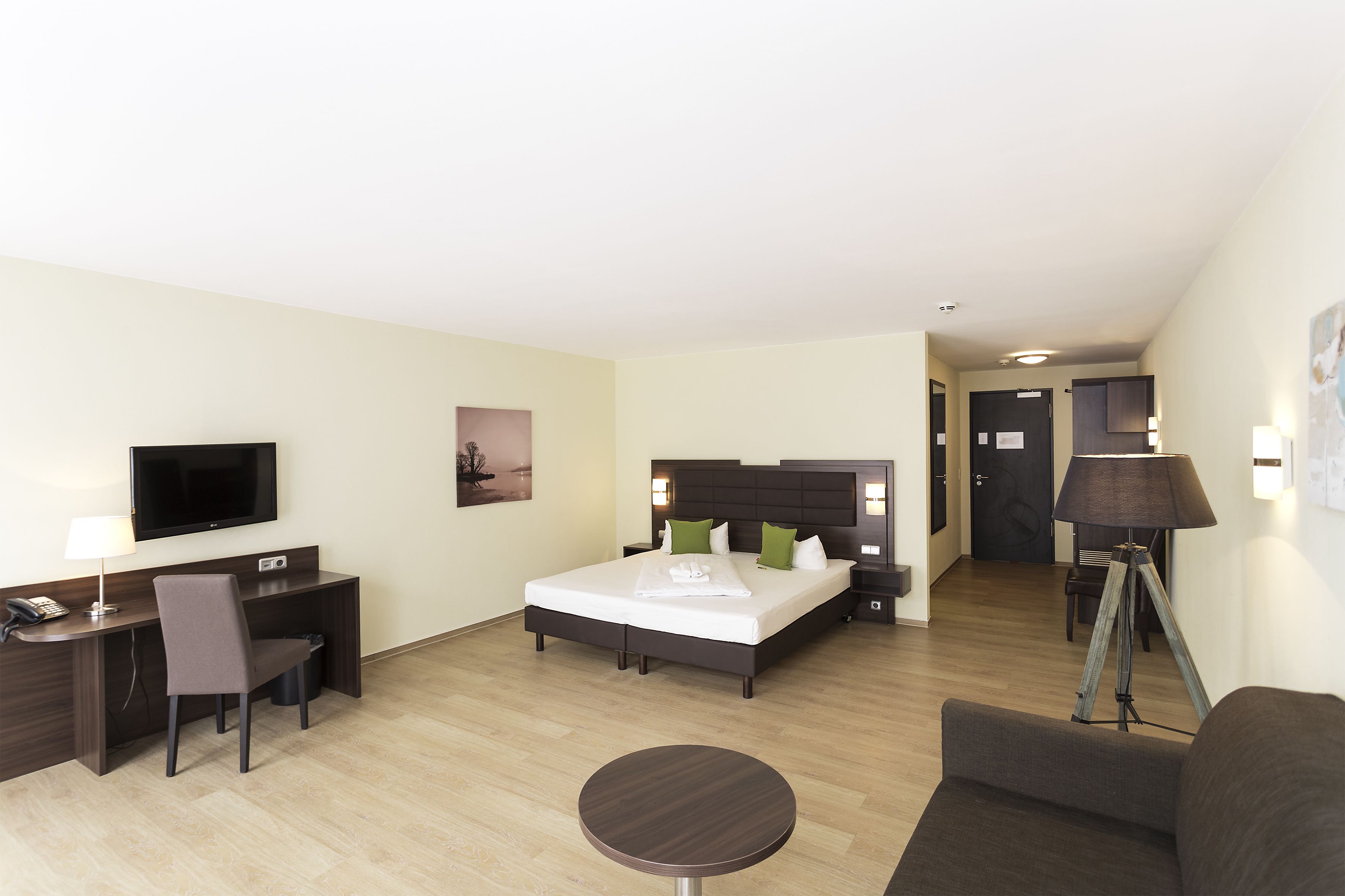A hotel room with a bed, desk, chair, TV, lamp, and a small table.
