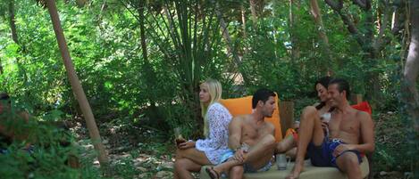 A group of people sitting on a circular wooden bench in a lush, green outdoor setting.