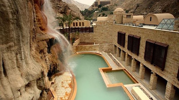 A pool area with a waterfall feature, stone walls, and a building with multiple windows.