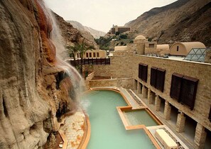 Un área de piscina con una cascada, paredes de piedra y un edificio con varias ventanas.