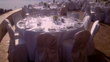 Mesa redonda dispuesta para un evento de cena formal al aire libre, con manteles y sillas blancos, con vistas a un paisaje pintoresco.