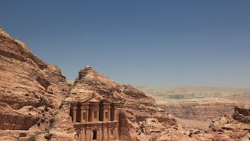 A large, ancient rock-cut structure with a central doorway, surrounded by rugged, reddish-brown cliffs.