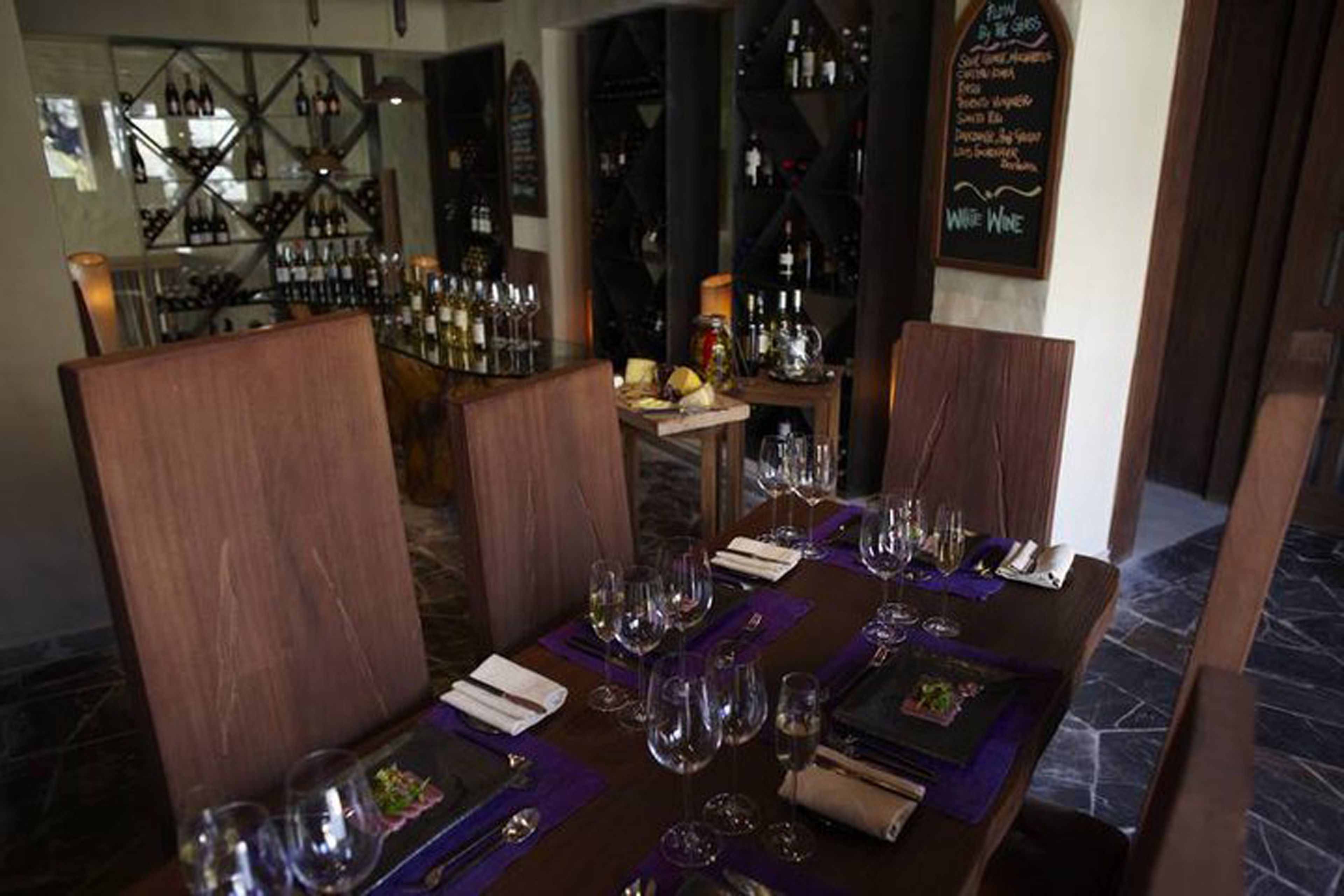 Un restaurante con una larga mesa dispuesta para comer, copas de vino y un panel con el menú al fondo.