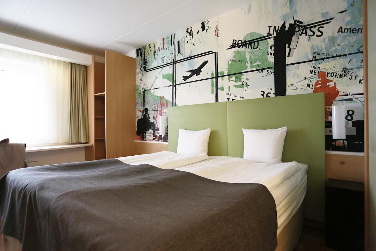 A hotel room with a bed, a desk, and a map on the wall.