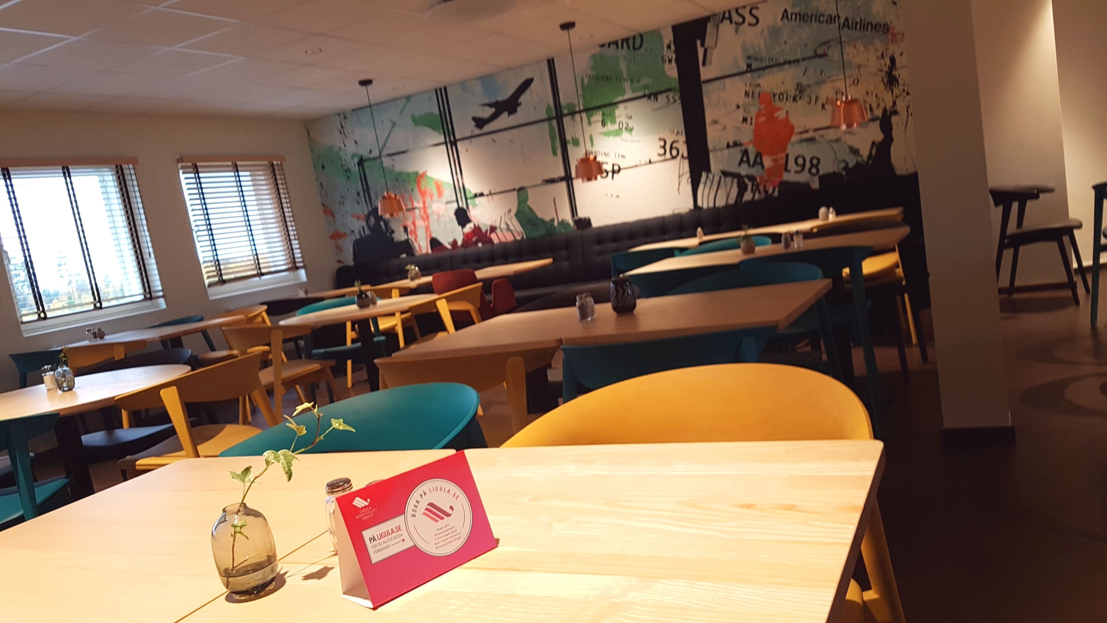 A restaurant with tables and chairs, a mural on the wall, and a window with blinds.