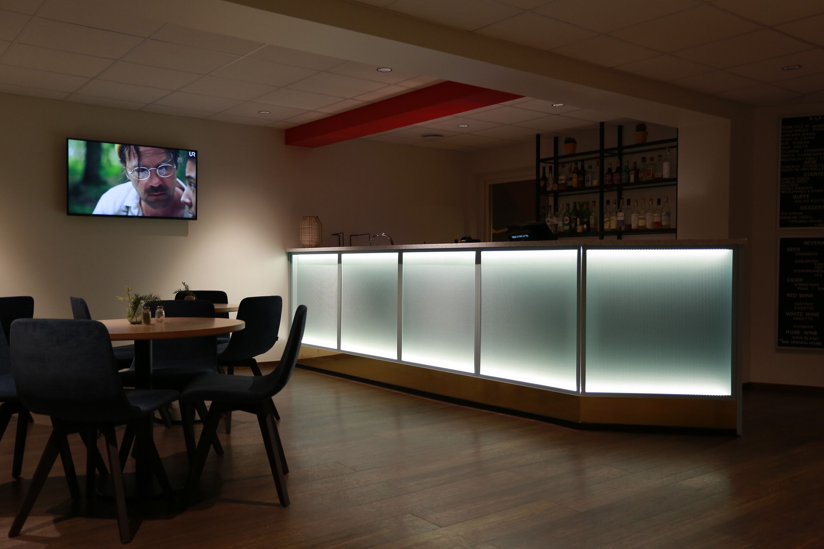 A modern bar area with a counter, chairs, and a TV screen.