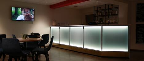 A modern bar area with a counter, chairs, and a TV screen.