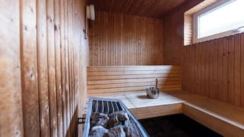 A wooden sauna with a bench, a bucket, and a stone-filled tray.