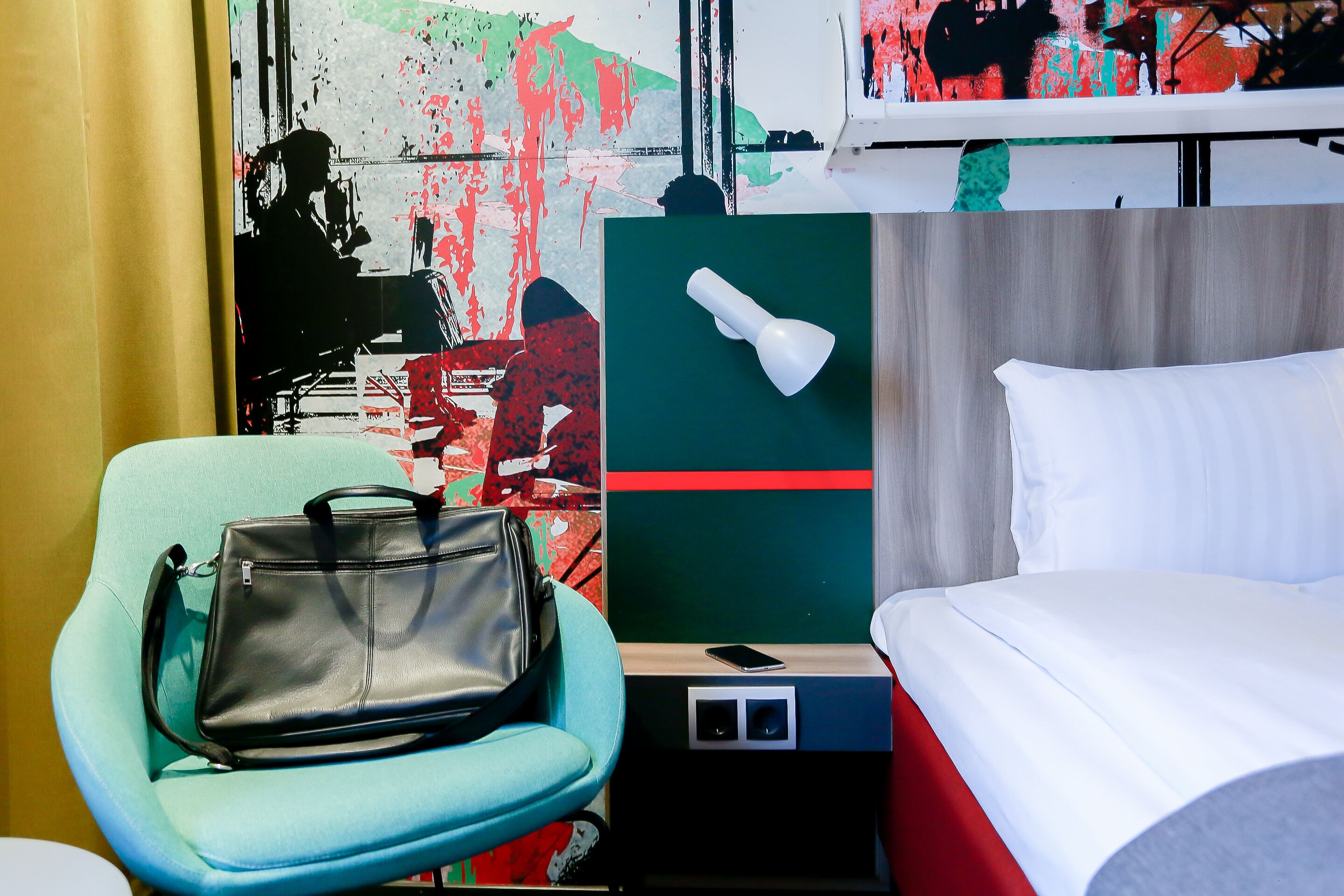 A hotel room with a bed, a chair, a desk, a lamp, and a painting on the wall.