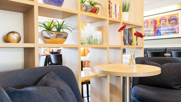 A modern interior with a round table, grey sofas, wooden shelving with books and plants, and a decorative bowl. - Good Morning Lund (Lund)
