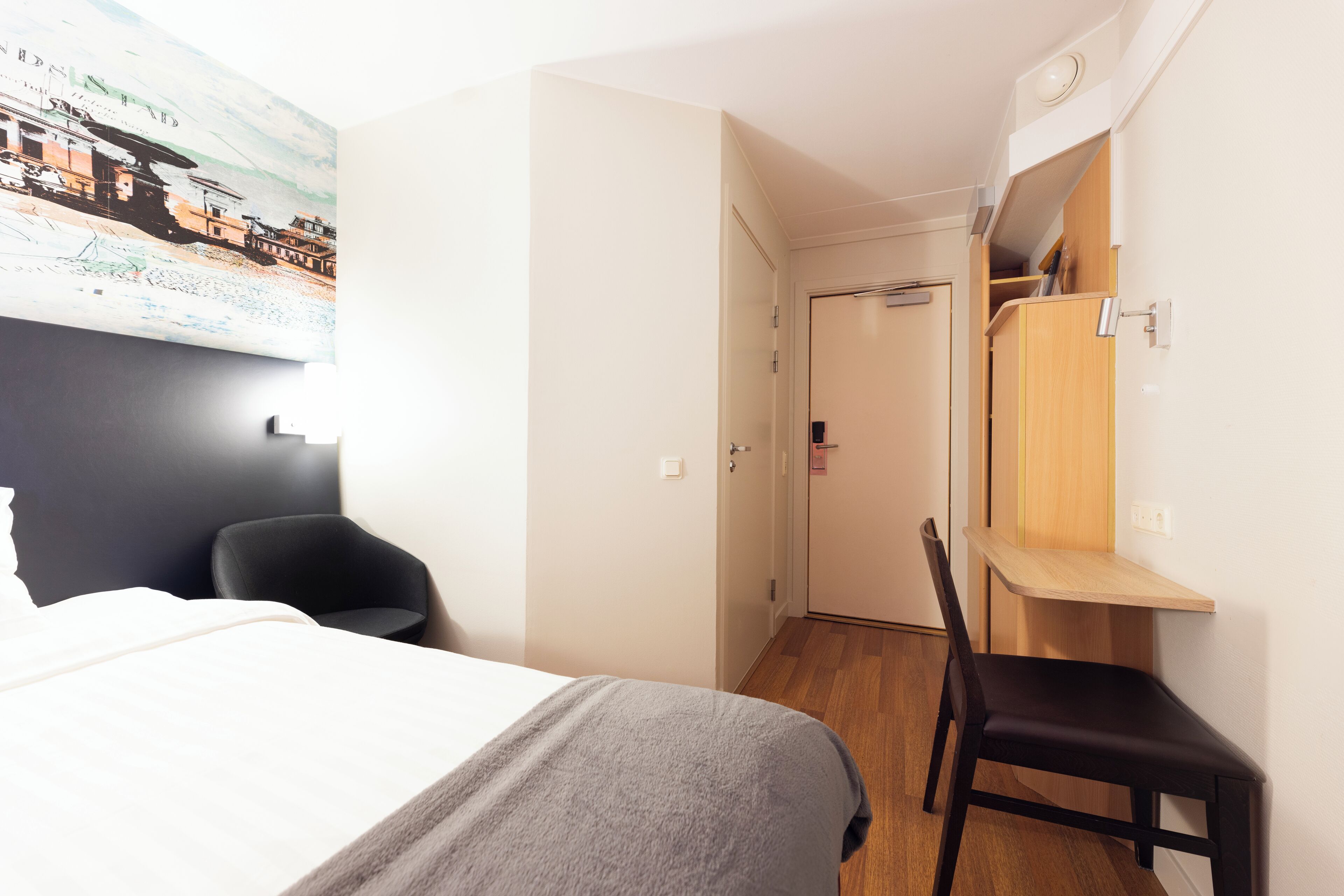 Una habitación de hotel con cama, una silla, un escritorio y un armario.