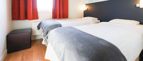 Habitación de hotel con dos camas, cortinas rojas, un cuadro en la pared y una mesita de noche negra.