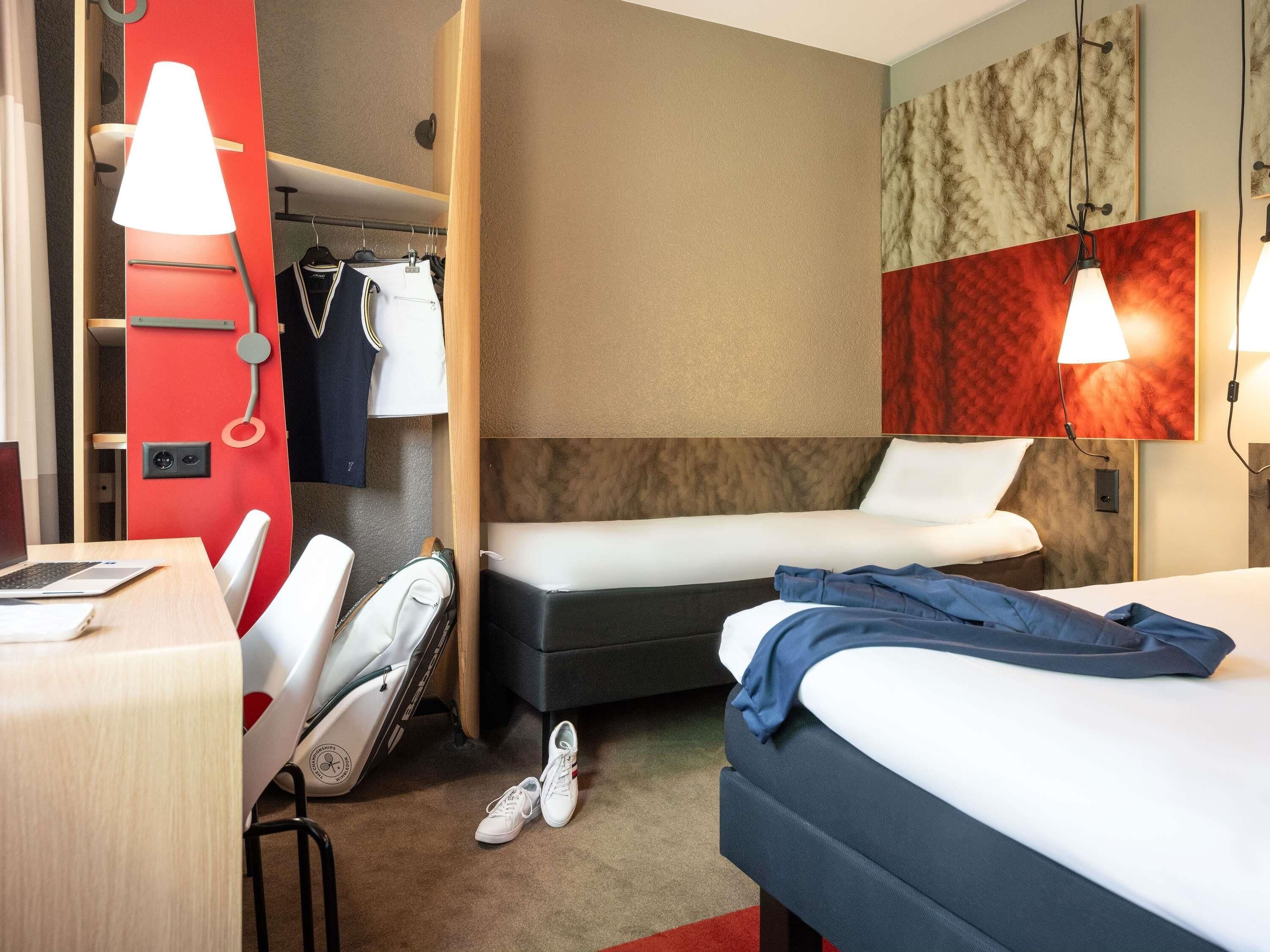 Habitación de hotel con cama, escritorio, silla, armario y espejo.