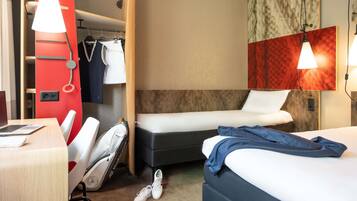 Habitación de hotel con cama, escritorio, silla, armario y espejo.