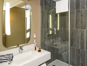 Ein modernes Badezimmer mit großem Spiegel, Waschbecken und Duschbereich.