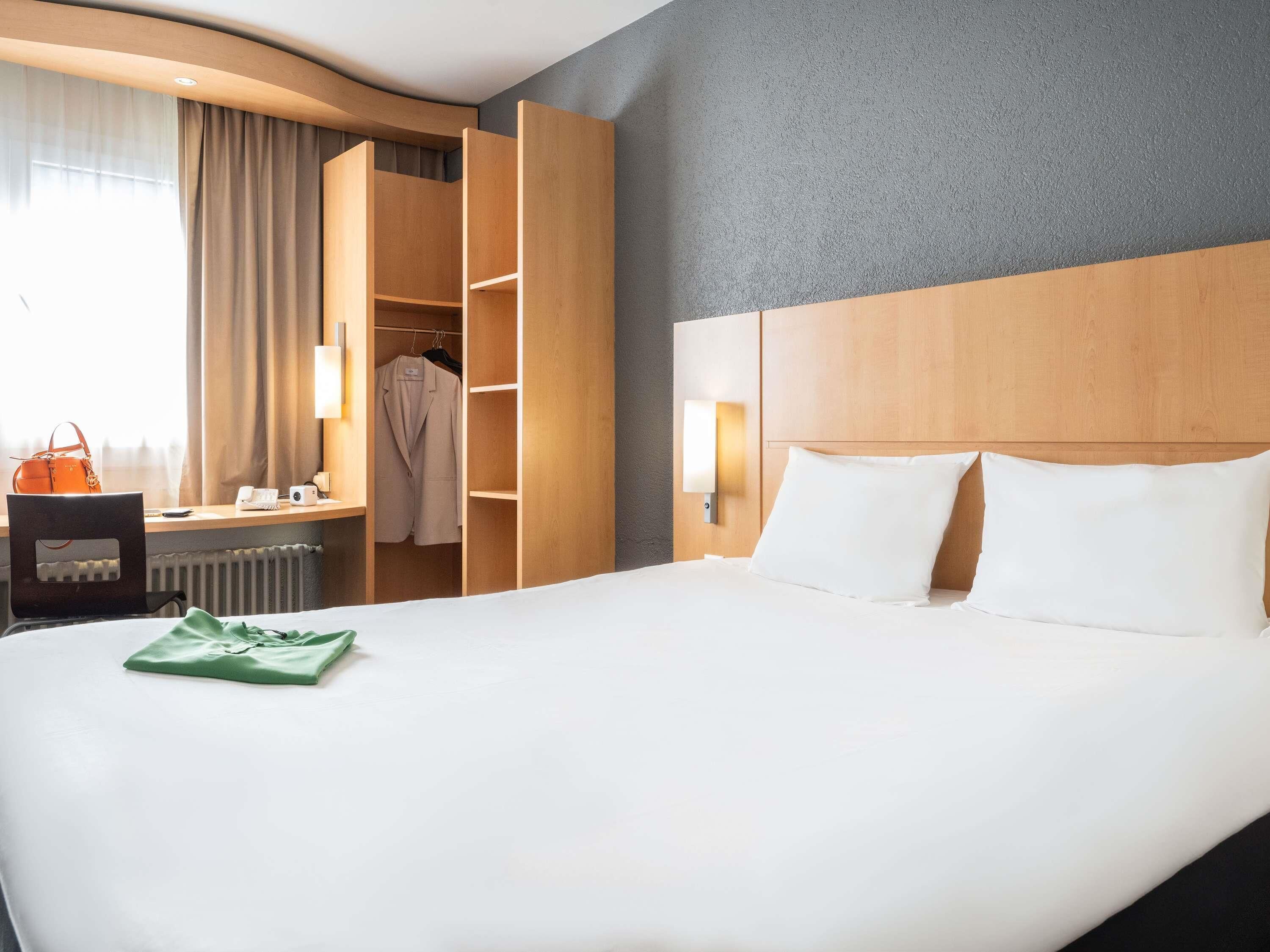 Quarto de hotel com cama, escrivaninha, cadeira, guarda-roupa e luminária.