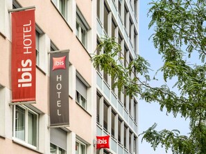 Un bâtiment d'hôtel orné de deux banderoles, une rouge et une noire, sur lesquelles figure le logo « ibis HOTEL ».