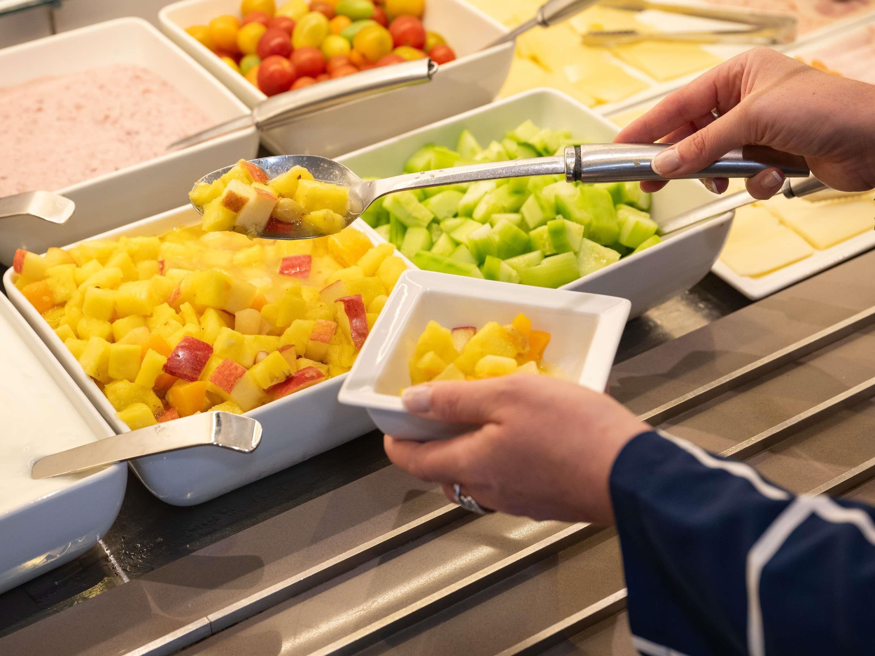 Ein Buffet mit verschiedenen Speisen, darunter Obst und eine rosa Nachspeise.
