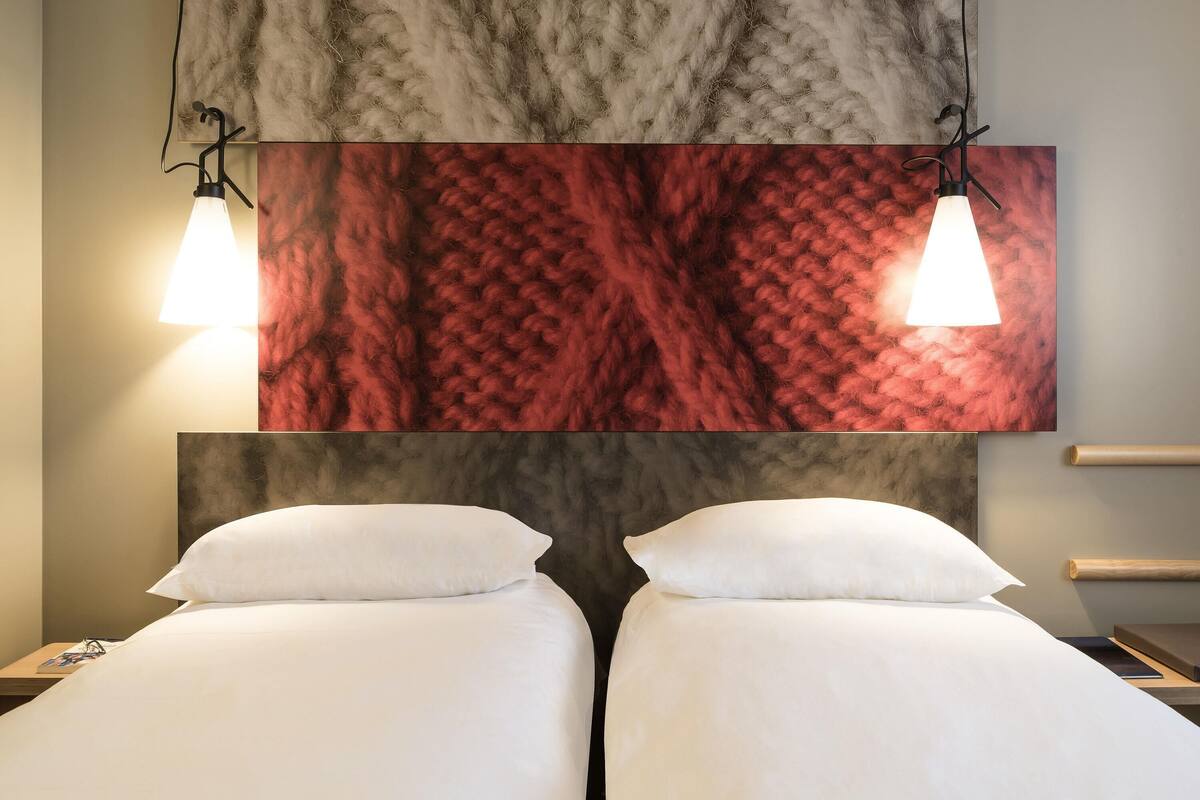 A hotel room with two beds, a marble wall, and pendant lights.