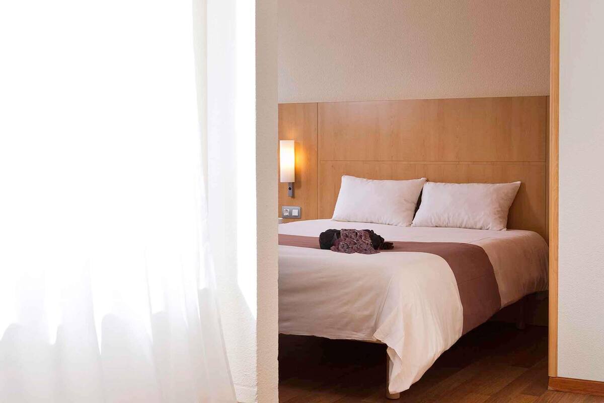 A hotel room with a bed, a nightstand, a lamp, and a wooden headboard.