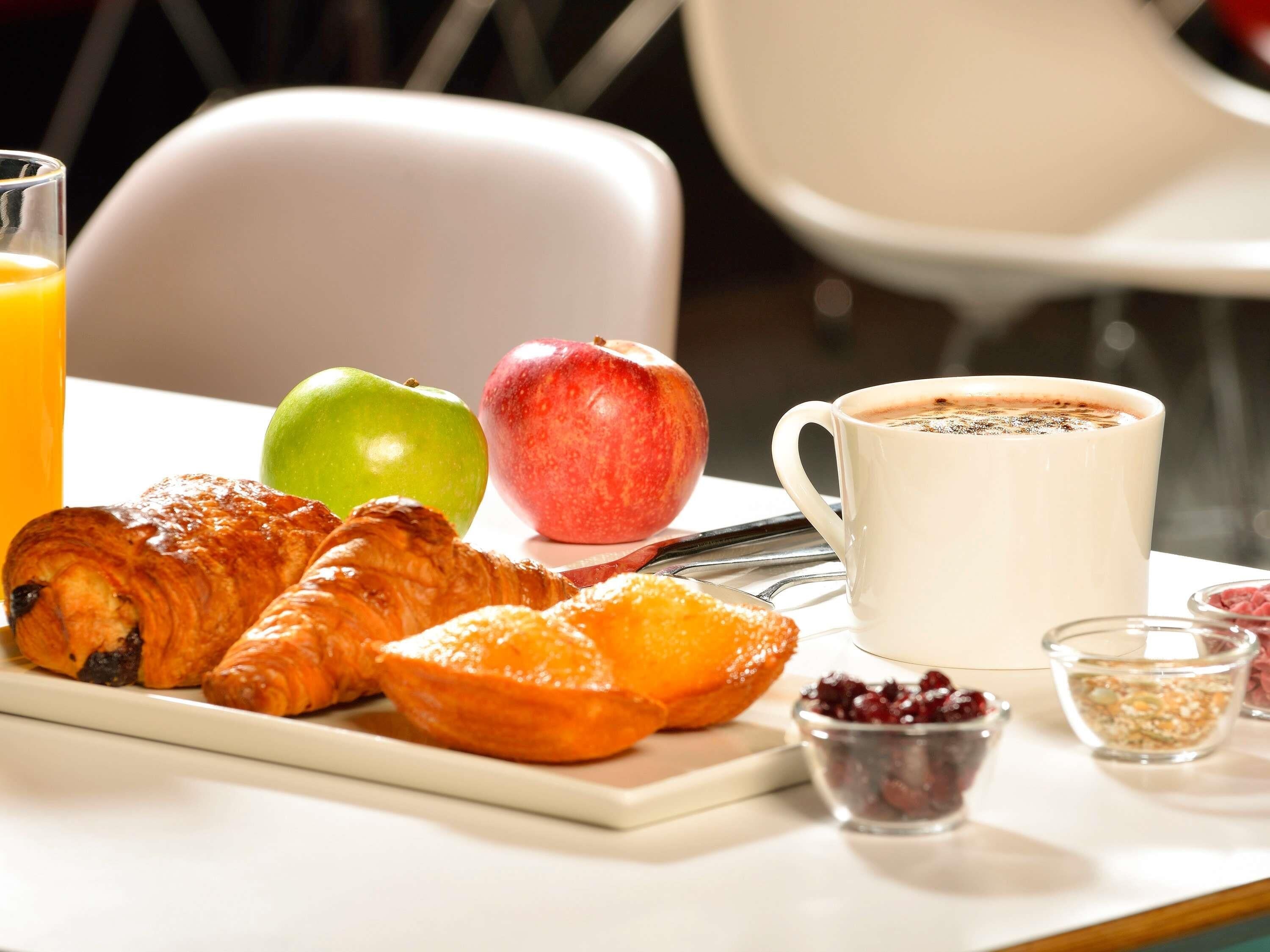 A breakfast tray with croissants, an apple, a glass of orange juice, and a cup of coffee.