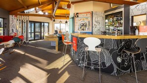 A bar area with a counter, stools, and a wall with abstract art. There is a seating area with a red sofa and chairs. The ceiling has exposed wooden beams. - ibis Angouleme Nord (Champniers)