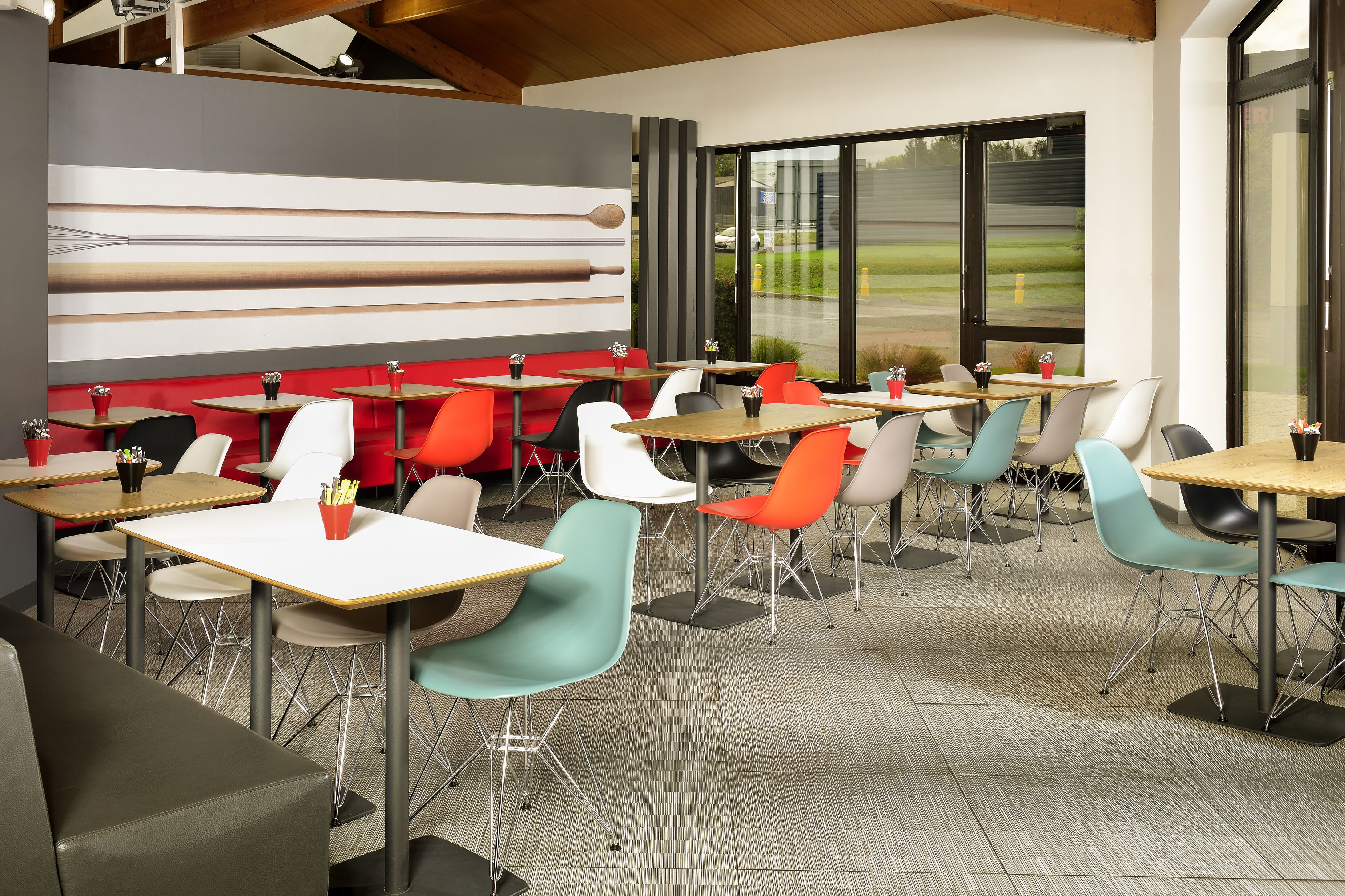 Un restaurant moderne avec un mélange de chaises rouges et turquoise, des tables en bois et un décor mural contemporain.