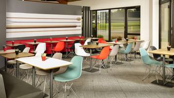 Un restaurant moderne avec un mélange de chaises rouges et turquoise, des tables en bois et un décor mural contemporain.