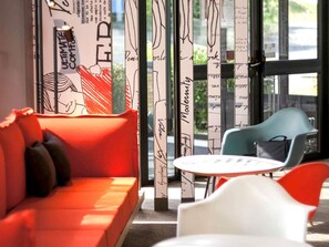 A modern interior with a red sofa, a white table, and a blue chair. - ibis Angouleme Nord (Champniers)