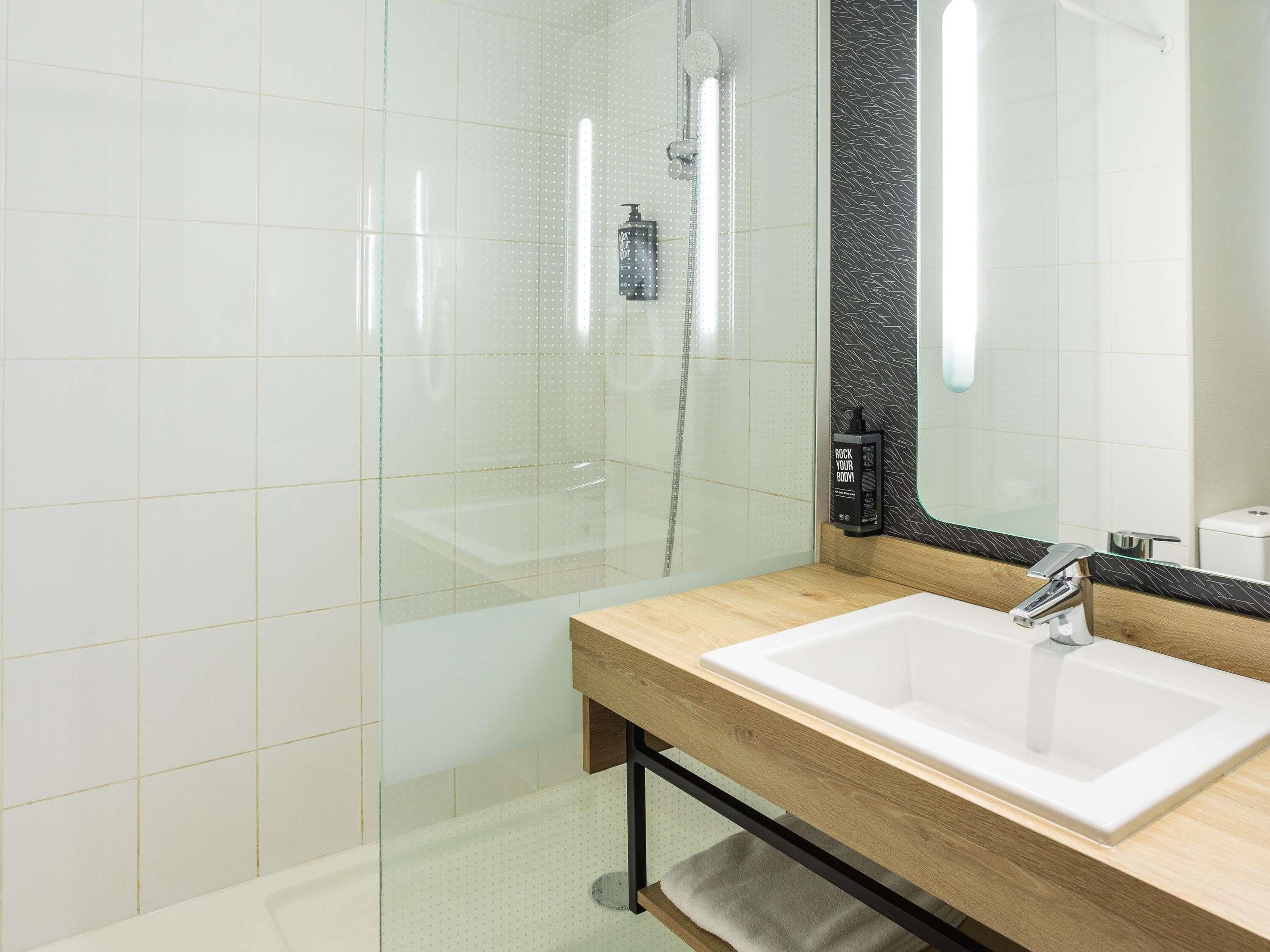 A modern bathroom with a glass shower enclosure, a wooden vanity with a white sink, and a large mirror.