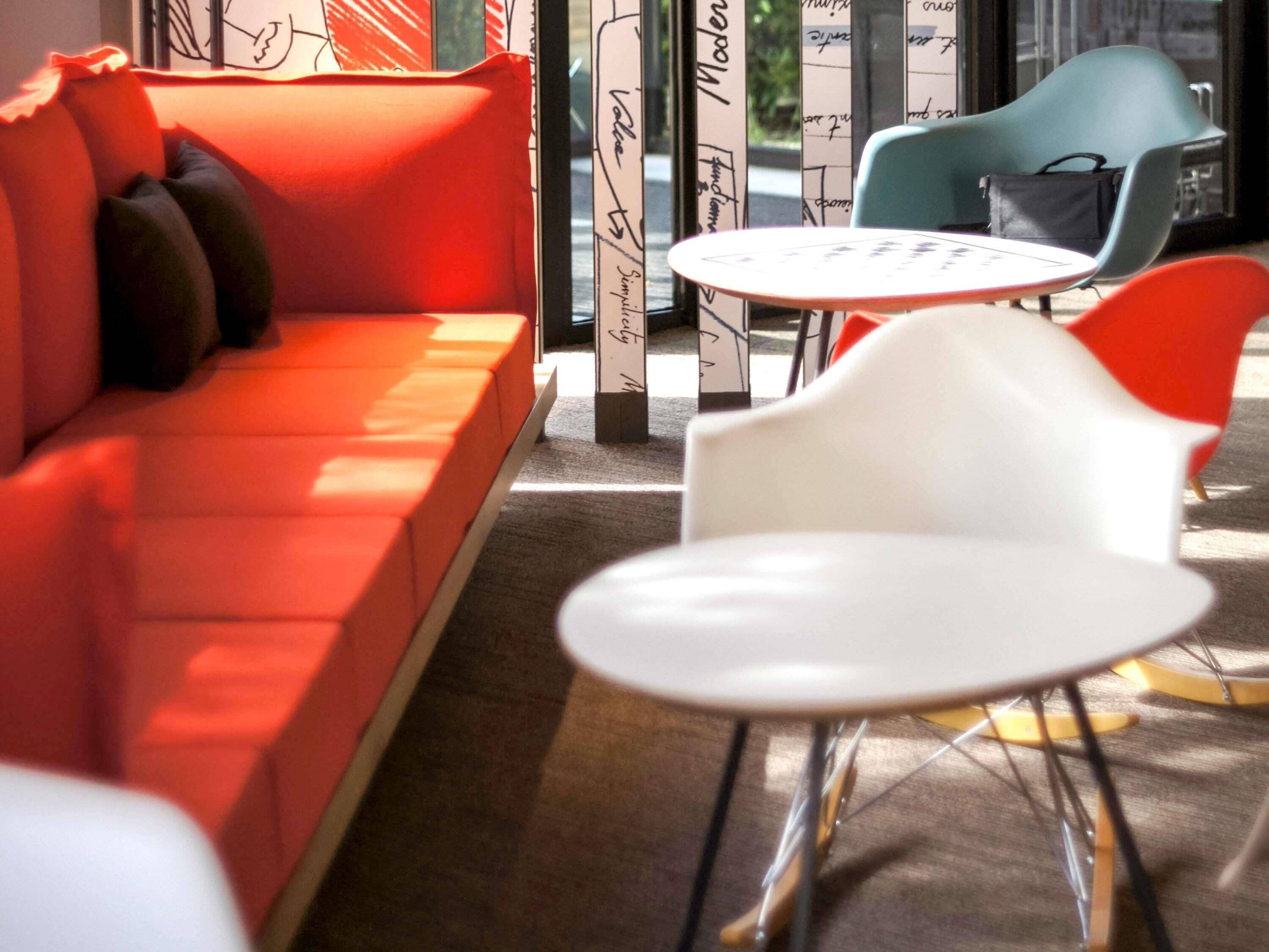 Un sofá rojo con cojines negros, una silla blanca y una mesa redonda en un interior moderno.