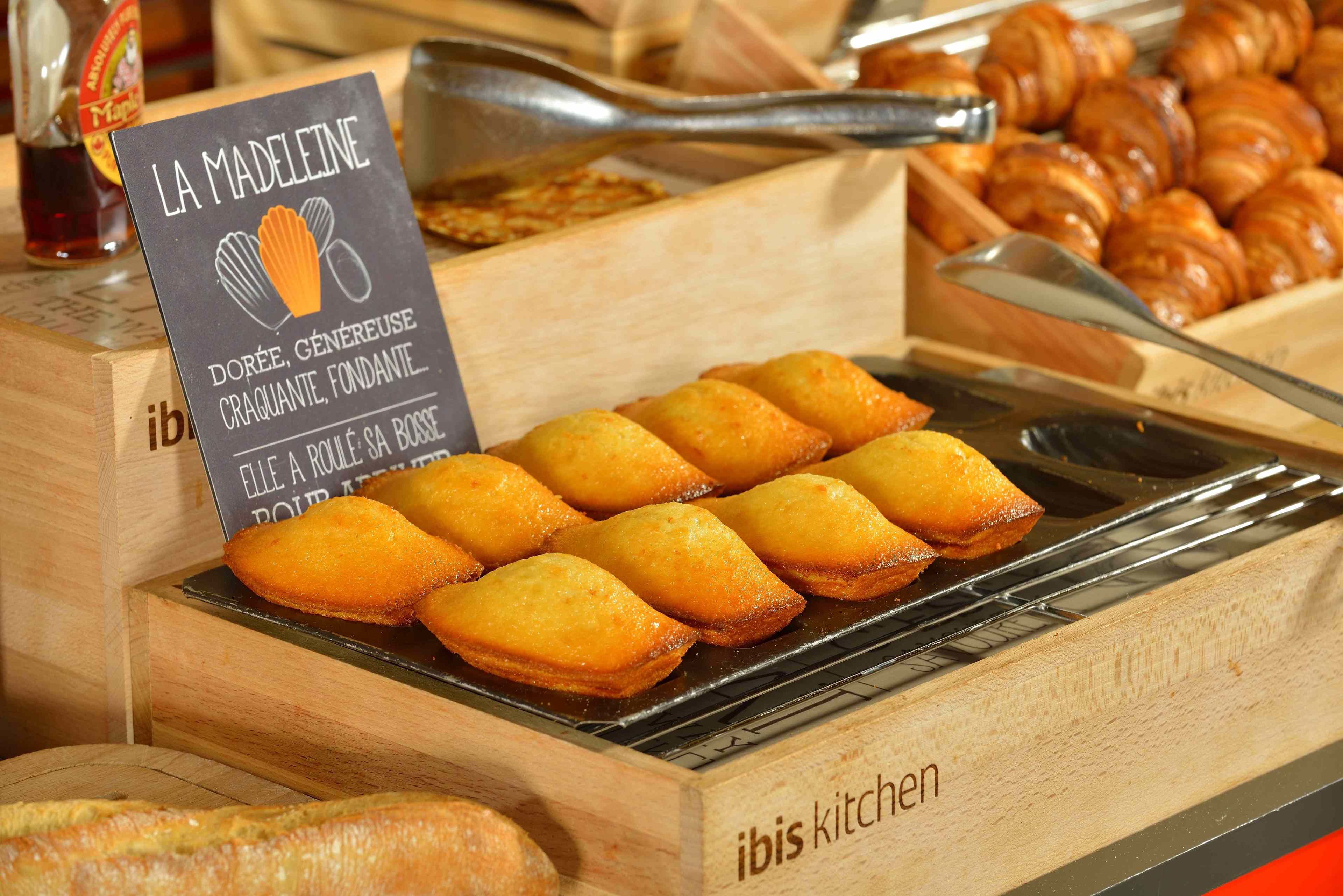 Une vitrine remplie de pâtisseries et une enseigne indiquant «La Madeleine», avec une boîte en bois et une pince à présentoir.