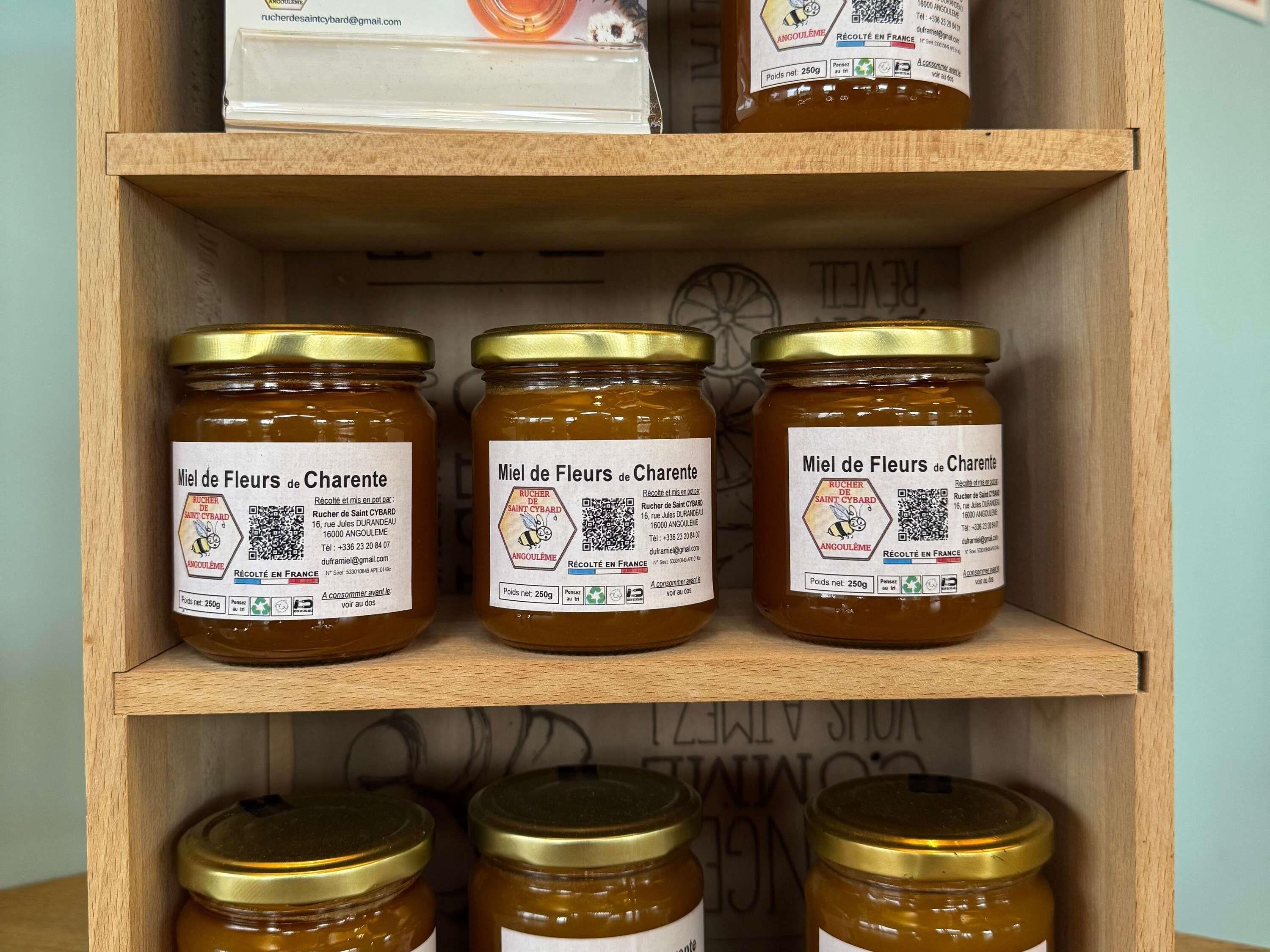 A wooden shelf with jars of 'Miel de Fleurs de Charente' honey, each labeled with the producer's name and address.